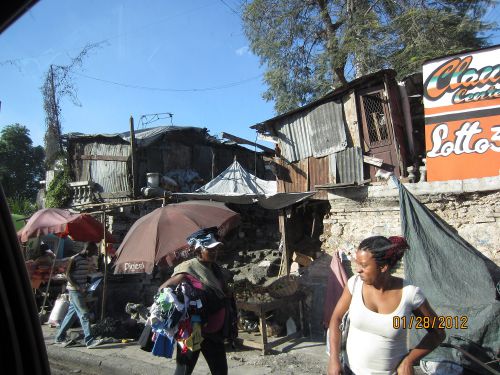 Dans Port-au-Prince, vendeuses sur la rue en avant des pauvres maisons - In Port-au-Prince, sellers on the street in front of the poor houses.