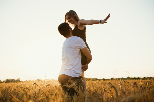 Deux amoureux enlacés devant un coucher de soleil dans un champ de blé